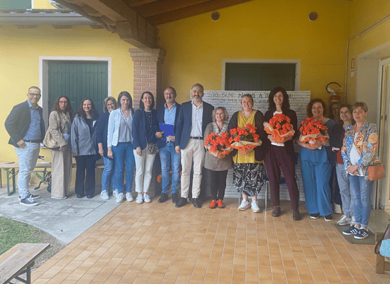 Gruppo di persone, educatrici e autorità nell'occasione di una ricorrenza. Alcune hanno un mazzo di fiori in mano