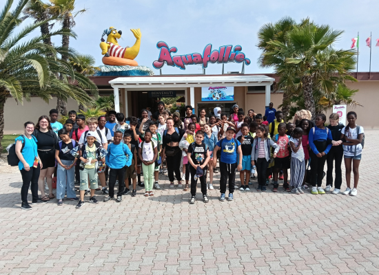 Foto di gruppo dei ragazzi e degli educatori del doposcuola davanti all’ingresso del parco acquatico Aquafollie di Caorle.