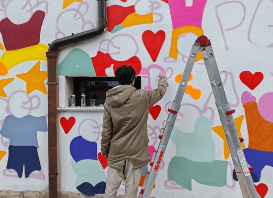 Giovane artista realizza un murale colorato con cuori e figure sul muro del Progetto Giovani Casarsa durante i festeggiamenti dei 30 anni.