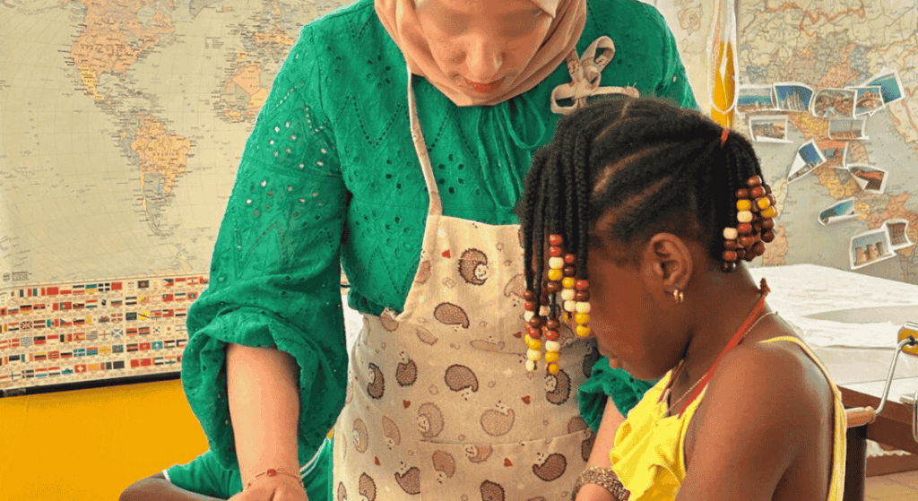 Donna con velo e bambina che partecipano a un laboratorio creativo del progetto Spazio alle Donne, accompagnate da una mappa del mondo sullo sfondo.
